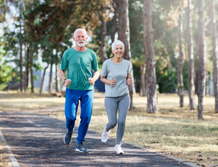 Obraz premium Smiling active mature senior couple jogging together in the park