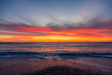 Obraz premium Dramatic Golden sunset over tranquil beach, waves lashing the pebble coastline