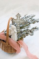 Fototapeta premium Palm Sunday background. wicker basket with pussy willow branches, christianity cross and angel figurine on light table. Easter, Palm Sunday holidays. prayer, faith, orthodox Church, religion concept.