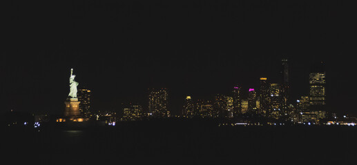 La icónica estatua de la Libertad iluminada de noche. Imagen tomada desde el ferry a Staten Island con el skyline de New Jersey al fondo en noviembre de 2019. © AngelLuis