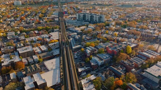 Aerial drone view of elevated train tracks running through a Brooklyn neighborhood with city skyline in the distance and autumn trees, filmed in ProRes 422HQ.