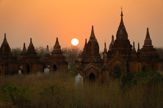 View of ancient temples silhouetted against the fiery sunset, their spires reaching towards the glowing orb in Old Bagan, Mandalay Region, Myanmar Burma.
