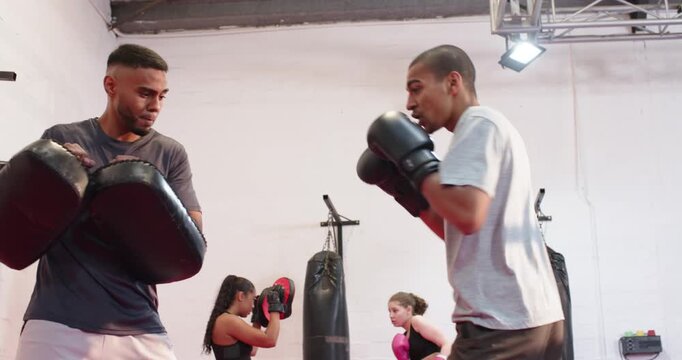 Male coach and trainee training with shifting pads in boxing gym as female trainees matching drills