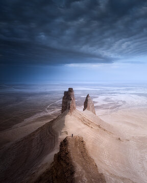 Aerial view of stark rock formations rise against a brooding sky, casting long shadows across the arid landscape, Aktau, Mangystau Region, Kazakhstan.