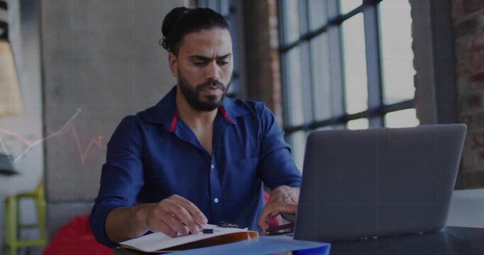 Man noting, flipping files then picking phone, scrolling, live graphs marking laptop for business