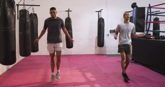 Male training partners picking up jump ropes and jumping in unison on boxing mat for cardio