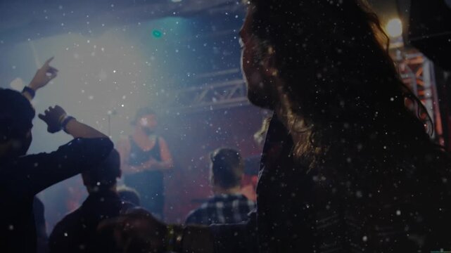 Crowd reacting to music starting men headbanging and pointing as stage light glaring over keyboard