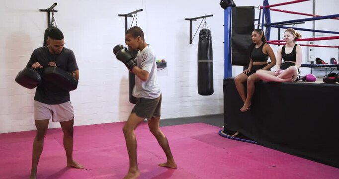 Male trainee and male trainer practicing punch and kick drills on mats following curved pad cues