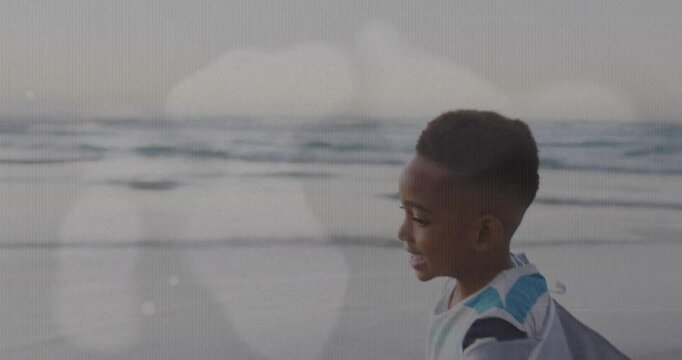 Boy smiling at camera running along beach for health reaching arm draping jacket bokeh overlaying