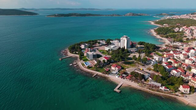 aerial panorama of Vodice coastline with Heksagon beach in the foreground, turquoise Adriatic Sea and dense town with marina in the background. Concept of Mediterranean destination, seaside cityscape