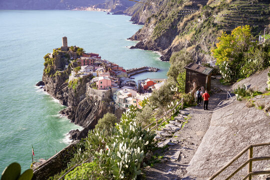 View of a coastal village clinging to dramatic cliffs, bathed in sunlight, where colorful buildings meet the turquoise sea in Vernazza, Liguria, Italy.