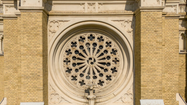 Aerial view of the intricate rose window of a church, a symphony of stone and light, casting shadows on the aged brick facade, Sad, Vojvodina, Serbia.