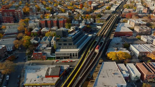 Aerial drone view of elevated train tracks running through a Brooklyn neighborhood with city skyline in the distance and autumn trees, filmed in ProRes 422HQ.