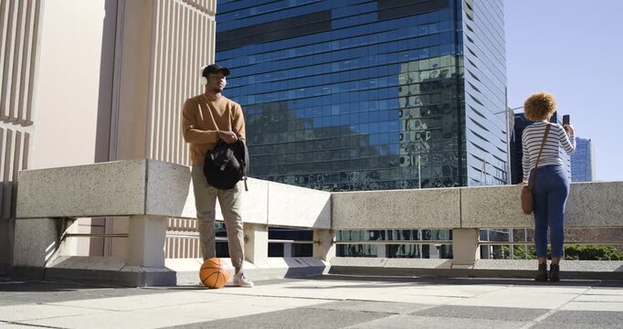 Diverse adults pausing on rooftop man checking backpack by basketball woman filming view with phone