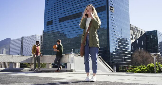 Woman answering phone, shielding and gesturing to attract attention in plaza with ball and suitcase