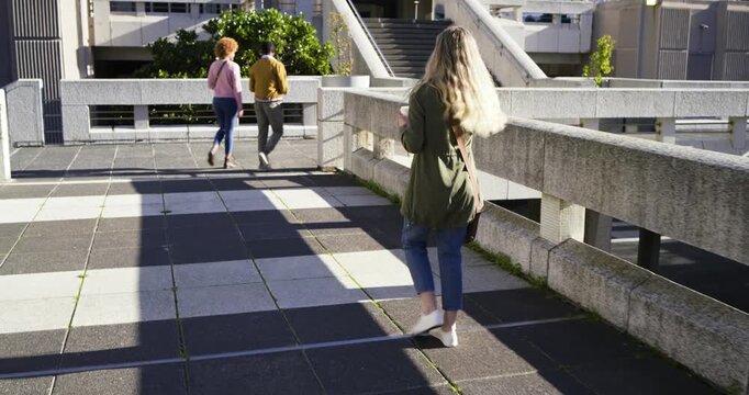 Blonde woman walking on raised urban terrace holding takeaway cup, following pair starting ascent
