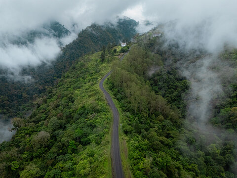 Aerial view of a winding road cutting through vibrant green forests, shrouded in mist, creating a serene and dramatic landscape., Cinchona, Alajuela Province, Costa Rica.