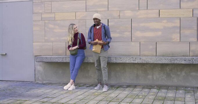Diverse friends smiling, man opening brown envelope by column while woman checking phone