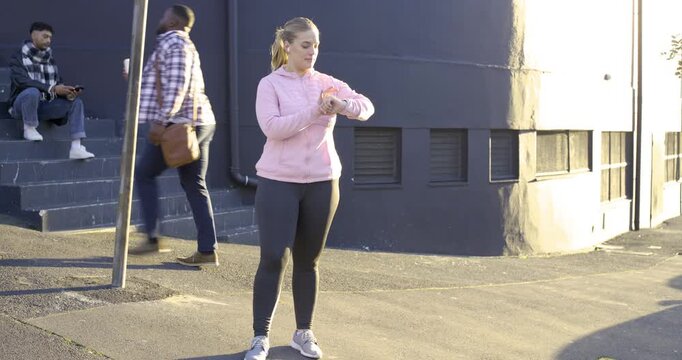 Adult woman in pink pullover checking watch, walking after man with coffee passing near dark wall