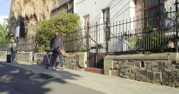 African American man pushing red-rimmed bike, avoiding drain on sidewalk and checking phone