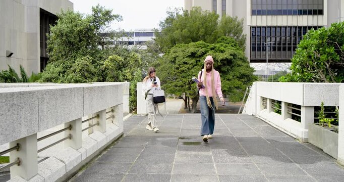 Diverse female students from bridge end walking to class, pink hoodie checking phone with binder