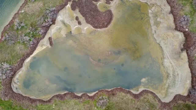 Cinematic top-down drone descending shot over a small coastal lagoon pond. High-angle view of unique water patterns and organic shapes. No audio. Ideal for nature and geography storytelling.
