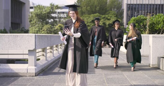 Female graduates celebrating taking selfie with phone and diplomas as friends walking up on campus