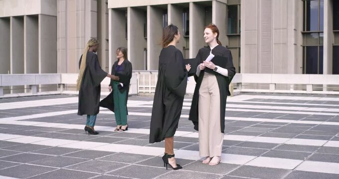 Diverse female classmates in gowns celebrating on plaza after getting diplomas, holding mortarboard