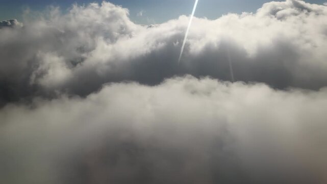 Aerial view: flyed on level of cumulus clouds in bright sun beams, fly into gray cloud. Natural cloudscape with sunbeams. Flying among cloudy sky. Flying inside cloud illuminated by sunshine