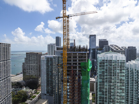 Aerial view of a towering yellow crane dominating the skyline amidst the high-rise buildings of Brickell, where construction meets the vast ocean, Brickell, Miami, Florida, United States.