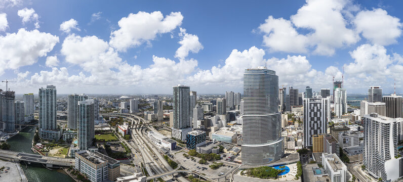 Aerial view of the sun-drenched Brickell cityscape, showcasing the winding Miami River and the bustling highways under a vast, cloud-dotted sky, Miami, Florida, United States.