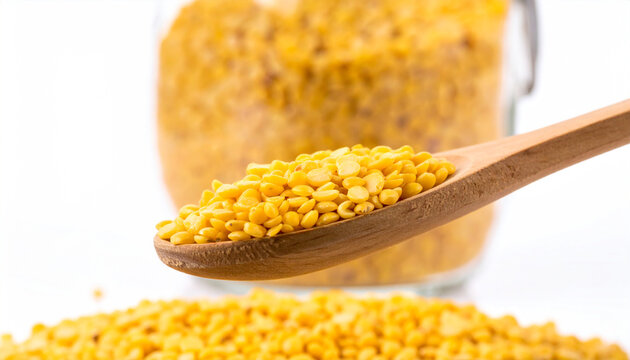 Wooden spoon with yellow split lentils in front of a blurred jar of lentils