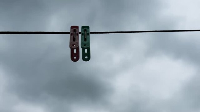 Two colorful plastic clothespins hanging on a wire against a dramatic overcast sky with dark rain clouds low angle view 4K video