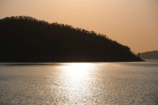 Golden Sunset Reflecting on Calm Sea with Forested Hill Silhouette