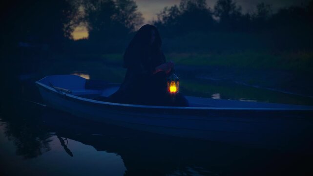 fantasy gothic woman floating in wooden boat down river night nature lightning way, hand holding lantern magic warm light. fairy elf girl sailing along lake fog dark forest tree. black dress hood cape