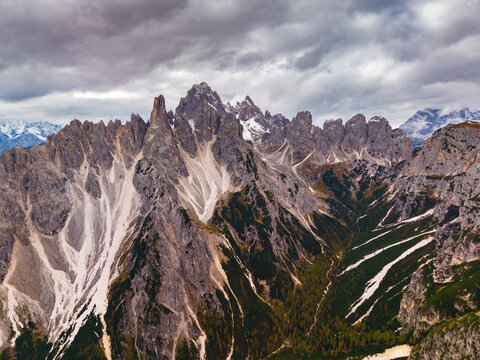 Aerial view of jagged peaks pierce the sky, their rocky faces etched with snow and shadow, a dramatic landscape unfolding beneath a brooding sky, Tre Cime di Lavaredo, Veneto, Italy.