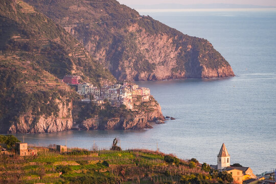 View of a charming Italian village nestled into the rugged coastline where colorful houses cascade down to the turquoise sea, Manarola, Liguria, Italy.