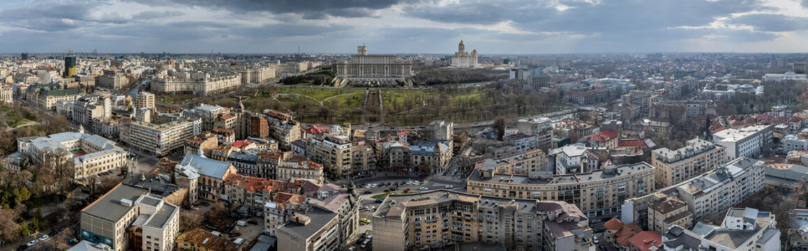 Aerial view of grand buildings stand tall amidst a sprawling urban landscape, framed by lush green spaces and a dramatic sky, Bucuresti, Bucuresti, Romania.