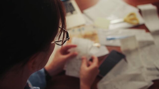 A woman calculates monthly expenses, for a period going through her purchase receipts and adding up on a calculator. Concept of a family budget. High quality 4k footage