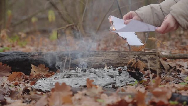 Female hand holding burning sheet of paper , closeup photo Paper held above smoldering ashes before ignition, concept of decision and final separation from past