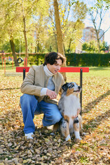 Fototapeta premium Young man enjoys a sunny spring day with his Australian Shepherd in the park