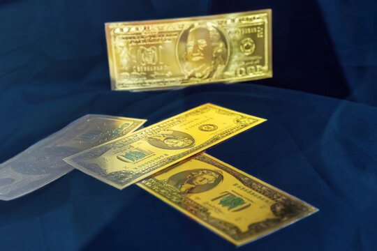 Golden souvenir one hundred dollar banknotes scattered on a dark blue fabric background.