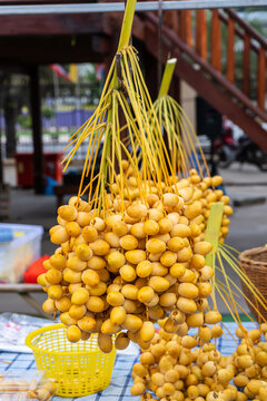 Bunches of fresh yellow Barhi dates hanging on a rack at a local fruit market stall.