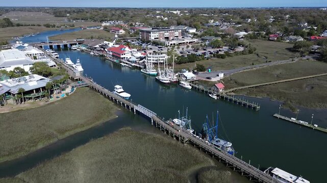 Marina pier alignment captures Shem Creek working waterfront near Coleman Boulevard with boats moored by busy dockside buildings. Glossy hulls, marsh grass, warm light coastal, Mt Pleasant, SC
