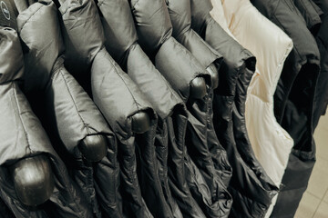 Neatly arranged collection of padded winter jackets and puffer vests hanging on a clothing rack © reddish
