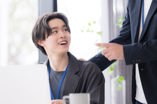会社の仕事中に上司に励まされる新卒などの新入社員の爽やかなイメージ　その調子！仕事頑張ってね！OJTで先輩に指導を受ける若手社員の成長と教育のビジネスシーン