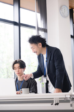 会社の仕事中に上司に励まされる新卒などの新入社員の爽やかなイメージ　その調子！仕事頑張ってね！OJTで先輩に指導を受ける若手社員の成長と教育のビジネスシーン縦
