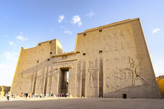 View of the majestic Temple of Horus, its weathered sandstone walls adorned with intricate carvings under a clear sky, standing as a testament to ancient civilization, Edfu, Egypt.