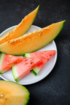 Melon slices and watermelon pieces arranged on a white plate against a dark background