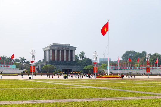 Hanoi, Vietnam - 18 January 2026: View of the solemn mausoleum standing proudly amidst the vast green expanse, framed by fluttering flags and ornate lampposts.